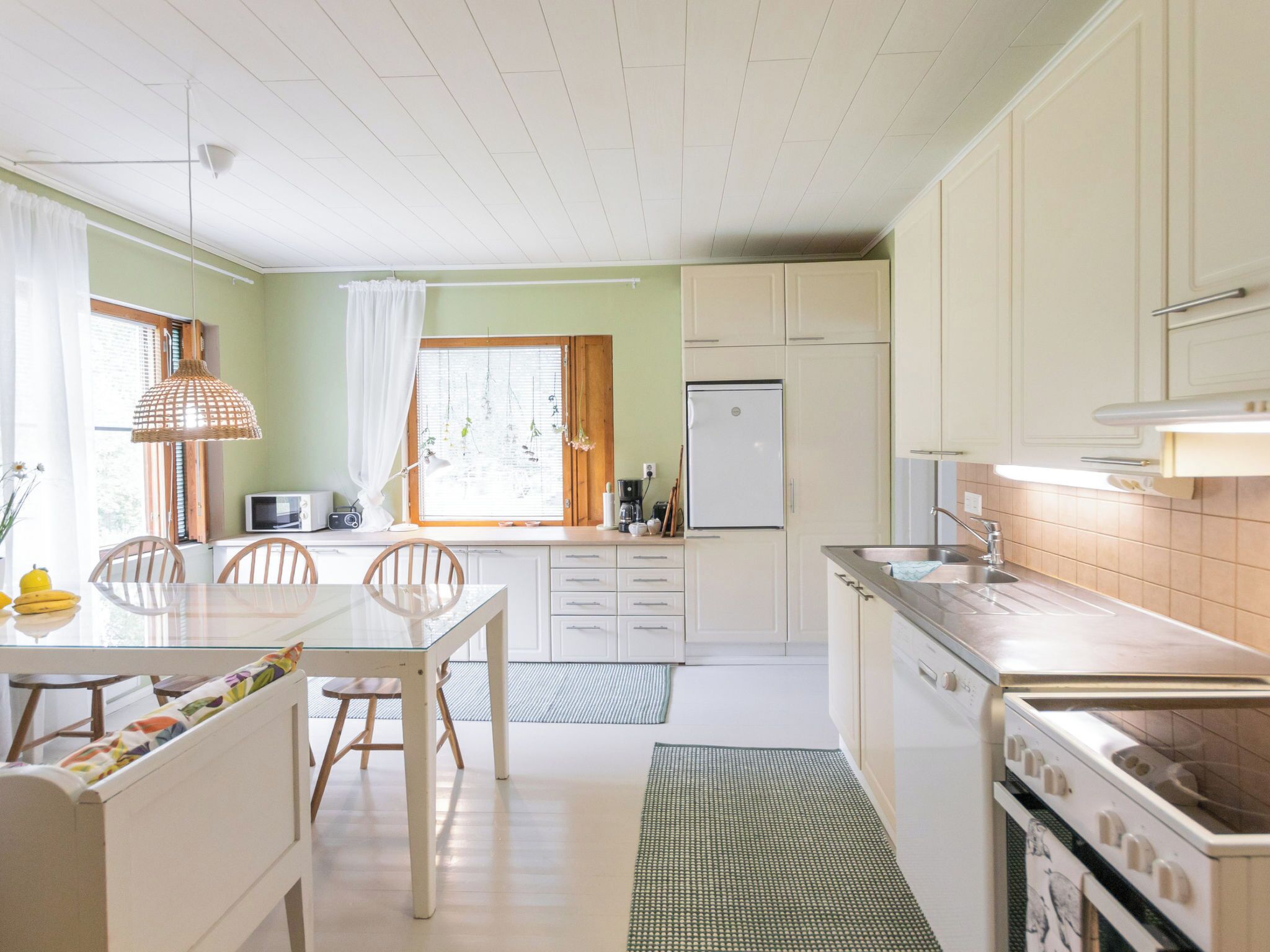 Ett kök med vita skåp, ett matbord med stolar, ett kylskåp och en spis.