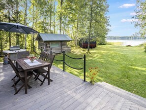 Una terraza de madera con una mesa y sillas, una parrilla y una construcción similar a una cabaña.