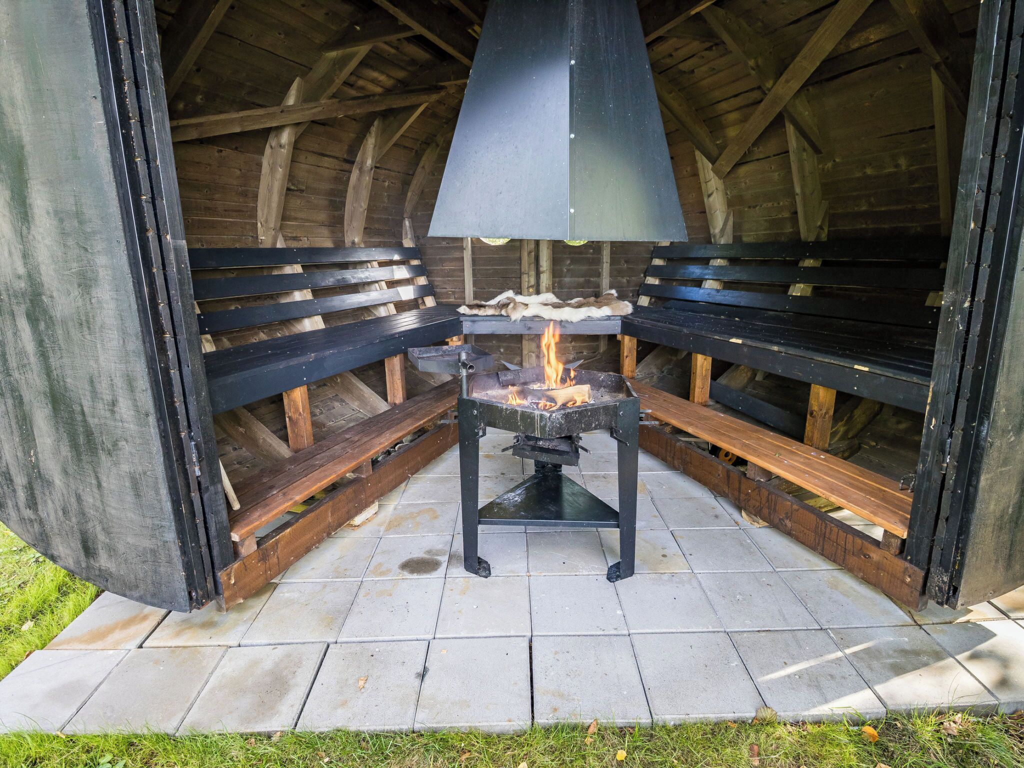 Een buitenkookplaats met een barbecue, banken en een betegelde vloer.