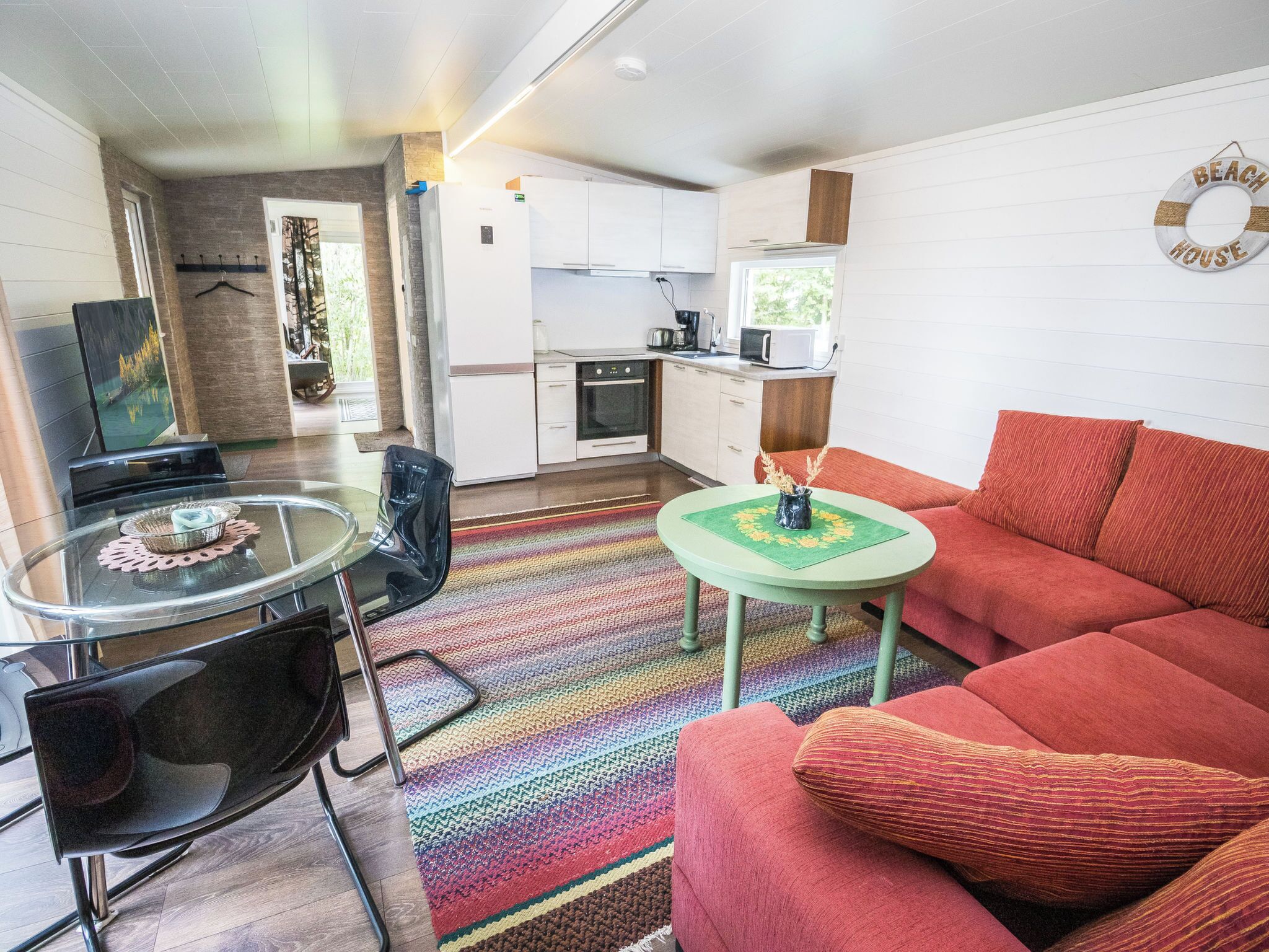 Een knus woongedeelte met een kitchenette, een eethoek met een glazen tafel en een bank.
