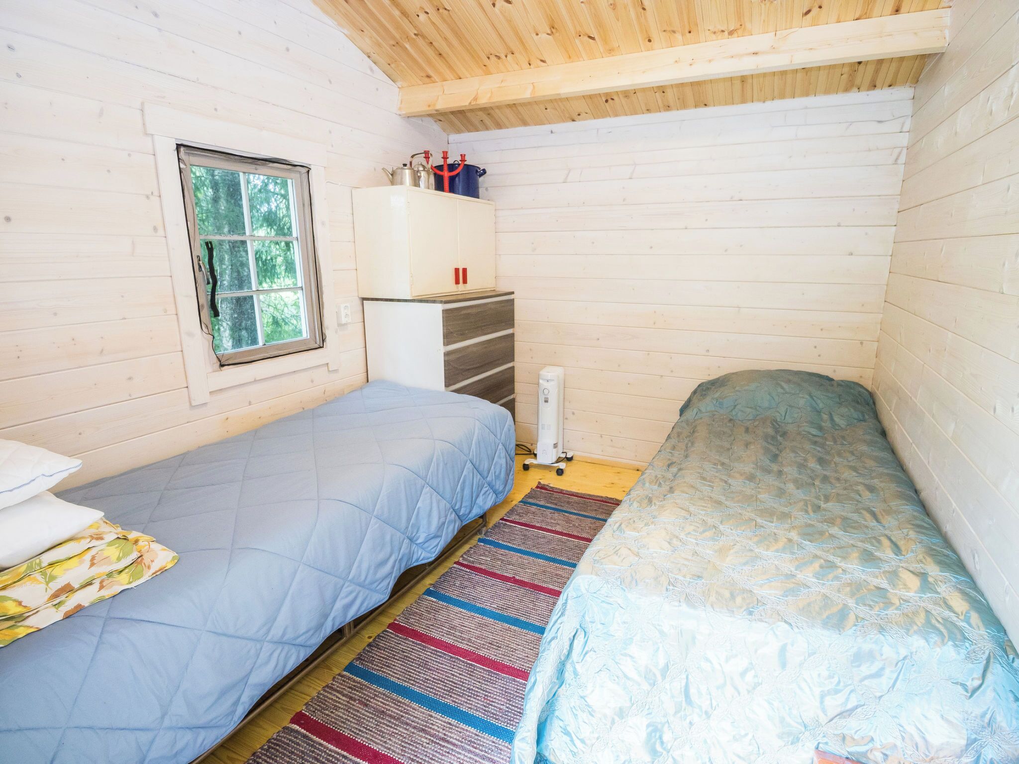 A small, cozy room with two beds, a window, a white cabinet, and a radiator.