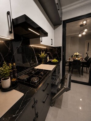 Een moderne keuken met een gasfornuis, zwarte kastjes en een eethoek met een tafel en stoelen.