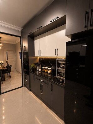 Eine moderne Küche mit dunklen Schränken, einer Marmorarbeitsplatte und einem sichtbaren Bosch-Kühlschrank.