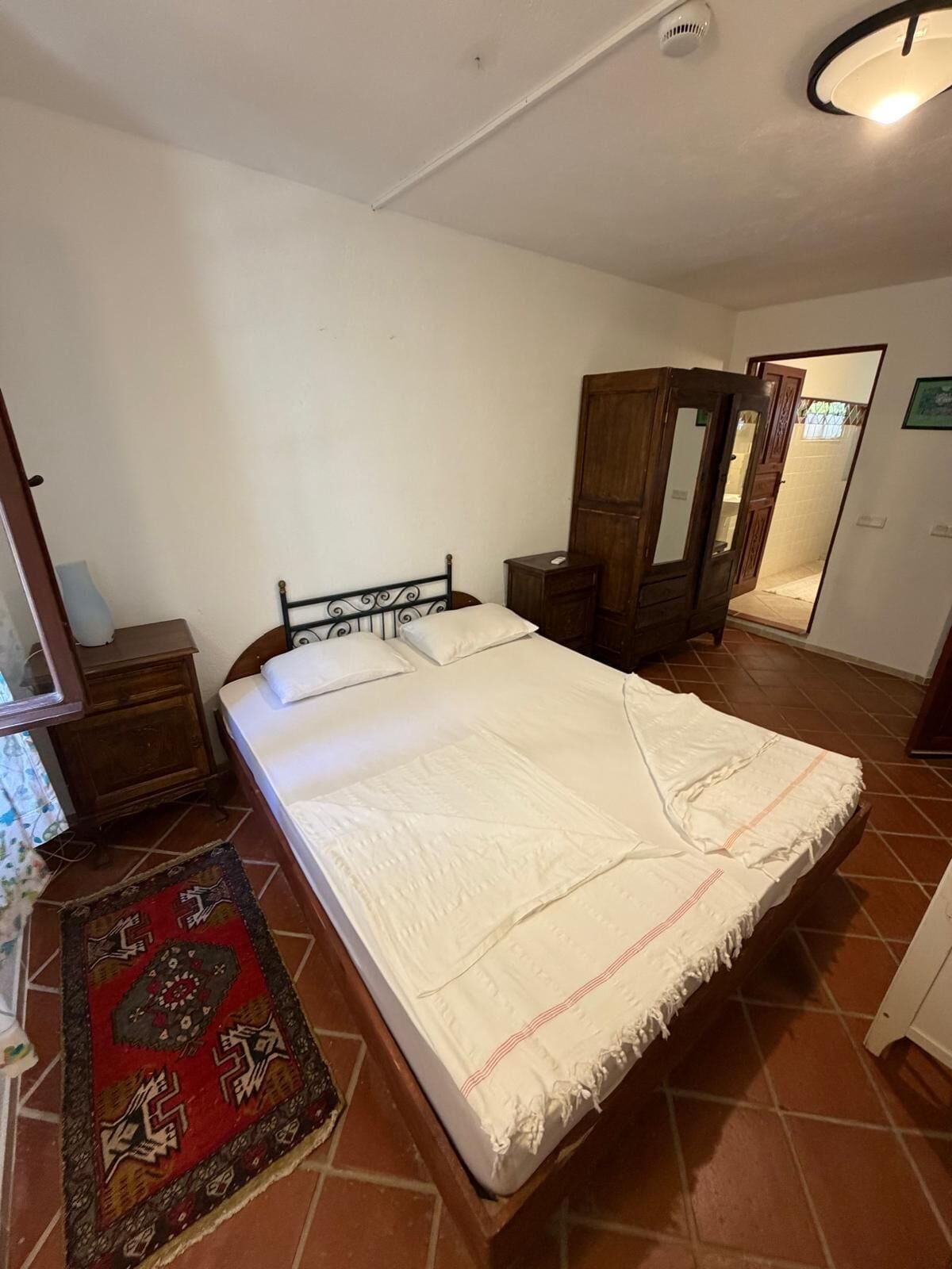 Een slaapkamer met een bed, een nachtkastje, een kledingkast, een spiegel en een kamerkleed met dessin.