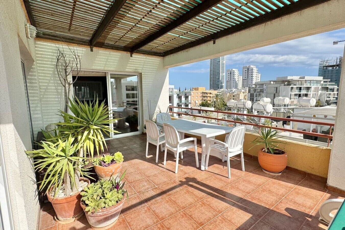 A balcony with a table and chairs, potted plants, and a city view.