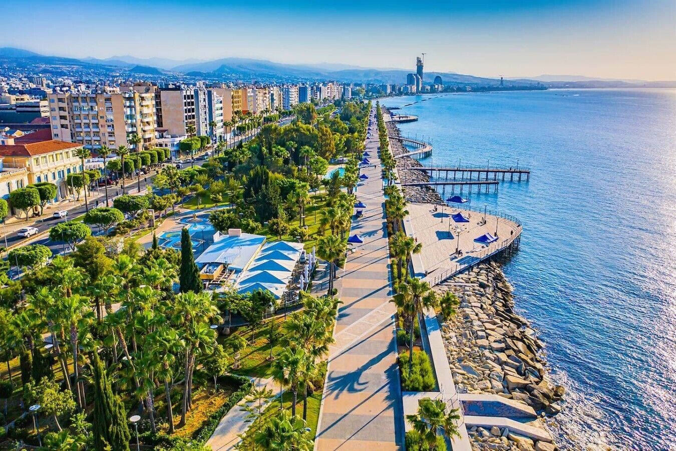 A coastal cityscape with a promenade, buildings, and a pier extending into the sea.