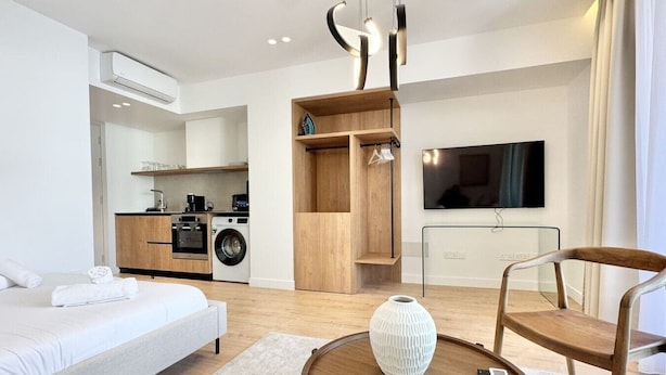 Quarto de hotel moderno com cama, sofá, mesa de jantar, cozinha e televisão.