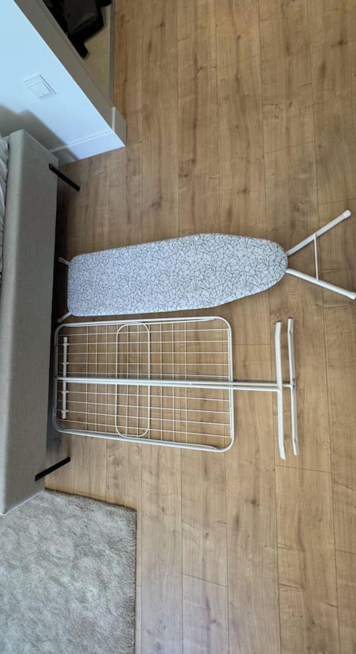 A room with a wooden floor, a metal drying rack, and a white wall.