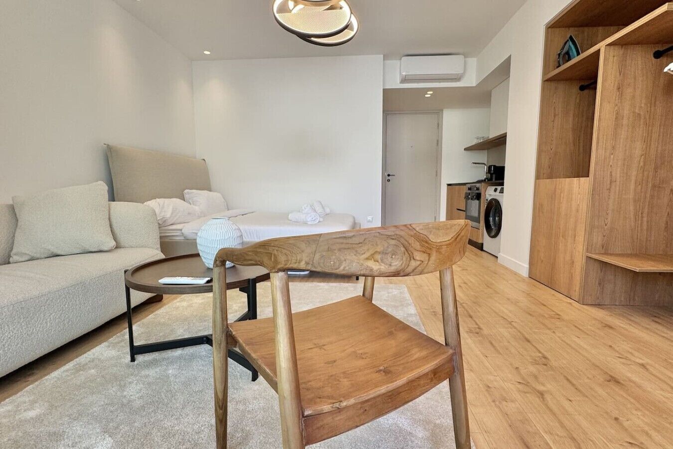 A modern living room with a wooden chair, a sofa, a coffee table, and a kitchen area in the background.