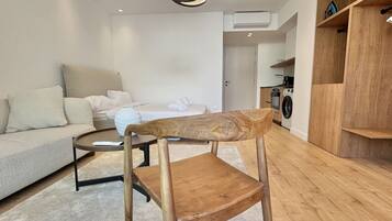 A modern living room with a wooden chair, a sofa, a coffee table, and a kitchen area in the background.