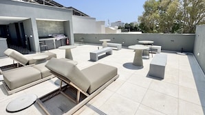 Terraço no telhado com espreguiçadeiras, mesas e área de churrasco.