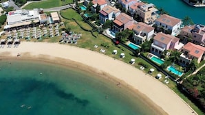 Vista aérea de uma área costeira com uma praia de areia, piscina e edifícios residenciais.