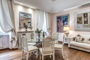 A dining area with a glass table, white chairs, and a white sofa. - Crispi Little Inn 1 (Roma)