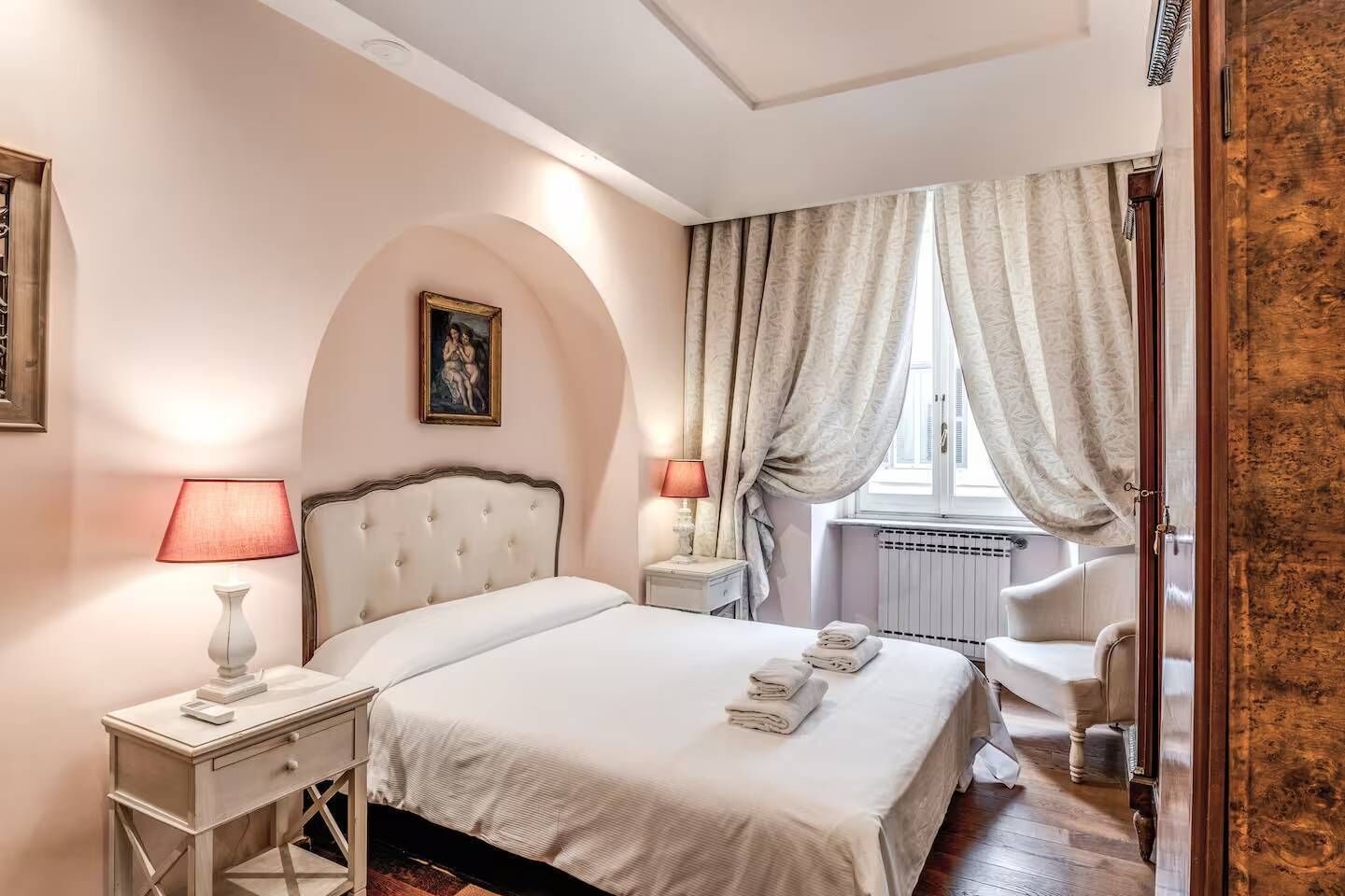 A hotel room with a bed, bedside tables, a window with curtains, and a radiator.