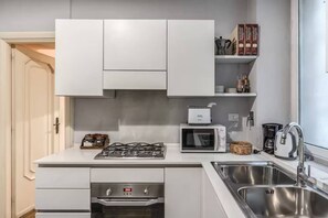 A compact kitchen with a gas stove, microwave, and built-in oven. There are cabinets above the counter and a shelf with kitchenware. - Crispi Little Inn 1 (Roma)