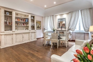 Ein geräumiges Wohnzimmer mit Holzboden, einem weißen Sofa, einem Esstisch mit Stühlen und einem großen Bücherregal voller Bücher und Dekoration.