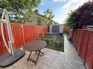 A patio with a round table and chairs, a shed, and a red wooden fence. - Triple Room (Shared House), Near Studios & Station (Watford)