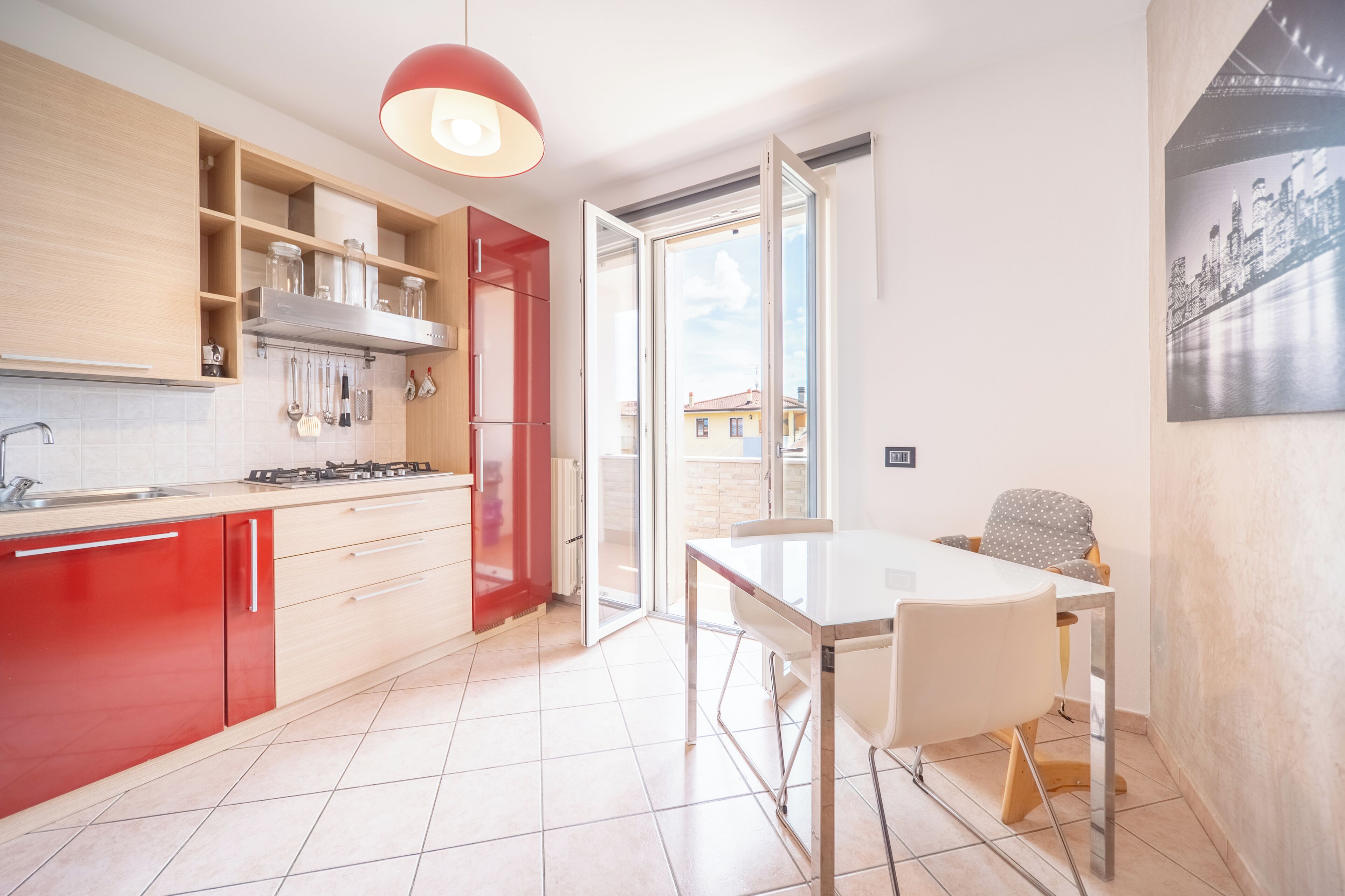 A modern kitchen with red cabinets, a gas stove, and a dining area with a white table and chairs.