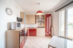Una cuina moderna amb armaris de fusta, un frigorífic vermell, una cuina de gas i un forn encastrat.