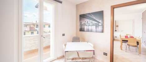 Una habitación con una mesa de comedor, sillas, un cuadro de un paisaje urbano y un ventanal corredero que da a un espacio exterior.