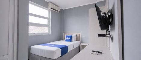 A hotel room with a bed, a desk, a TV mounted on the wall, and an air conditioning unit.