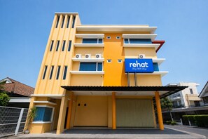 A modern hotel with a yellow facade, a sign reading 'Rehat Sleep Well Sleep,' and a covered entrance.