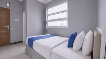 A hotel room with a bed, a window with curtains, a door, and an air conditioning unit.
