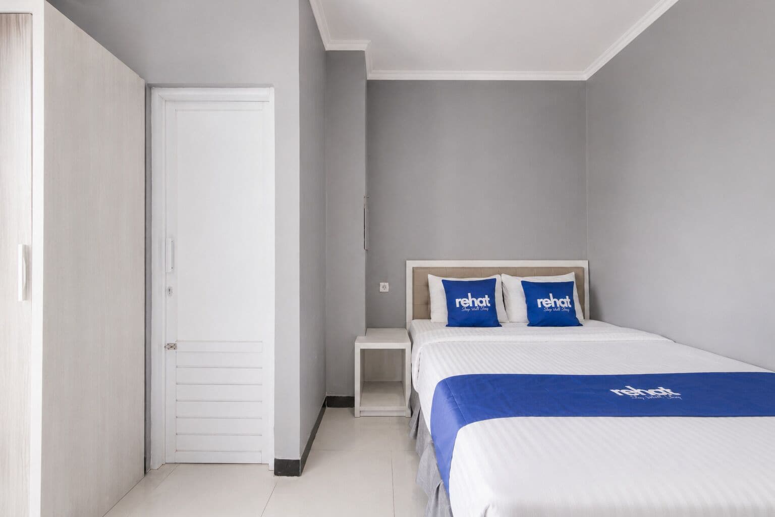 Une chambre d’hôtel avec un lit, une table de chevet, une armoire et une porte.