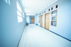 A long, narrow hallway with a tiled floor, large windows on one side, and doors on the other.