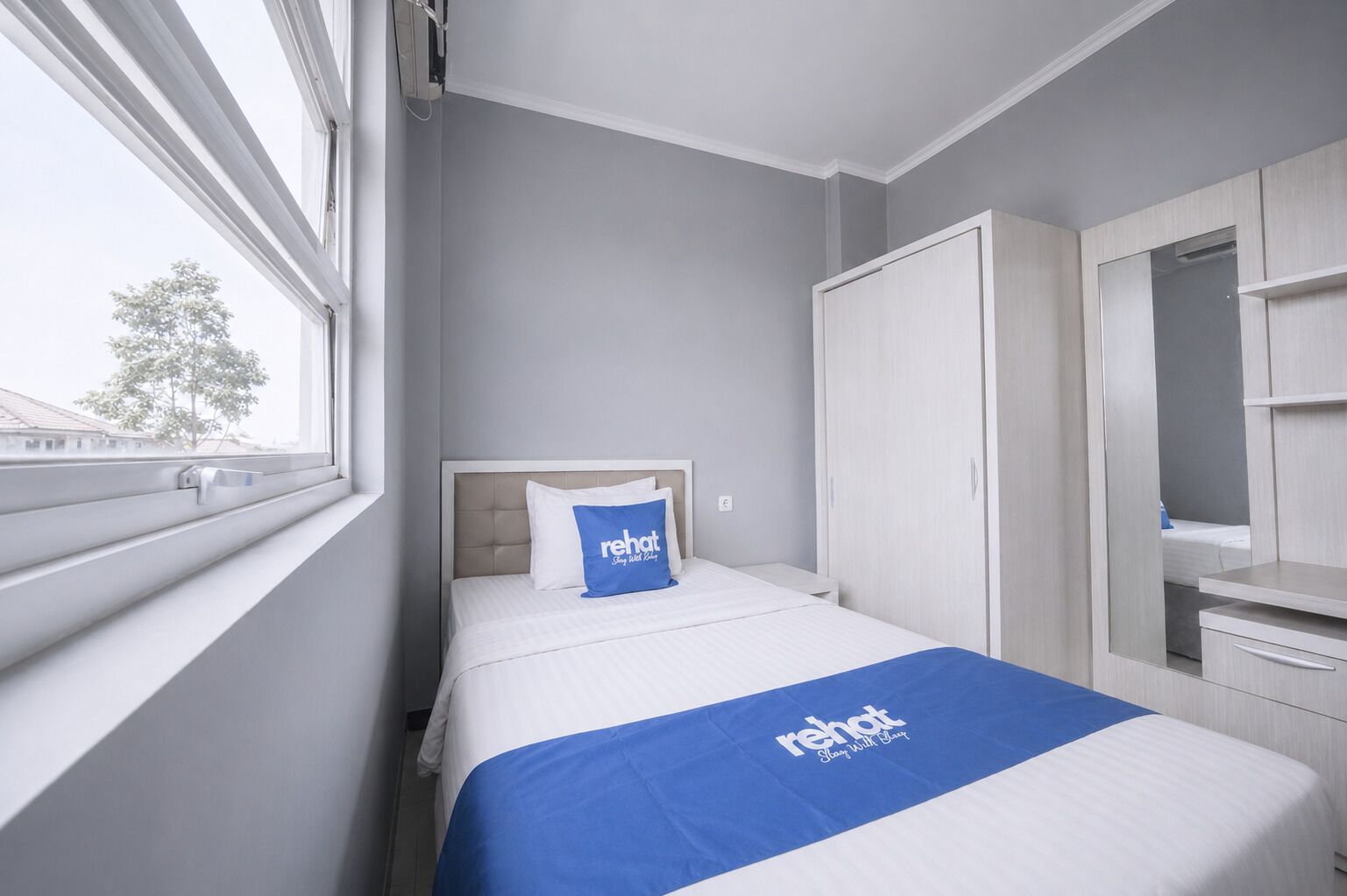 A hotel room with a bed, a wardrobe, a mirror, and a window.