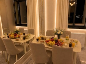 A dining area with a table set for four, featuring a fruit and juice arrangement, candles, and a vase with flowers. - Premium Apartment | 5 Min to Airport (Тоshkent)