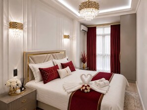 A well-appointed bedroom with a large bed, a bedside table, a nightstand, a chandelier, and a window with curtains. - Premium Apartment | 5 Min to Airport (Тоshkent)