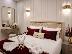 A hotel room with a large bed, a bedside table, a nightstand, a mirror, and a wall-mounted light fixture. - Premium Apartment | 5 Min to Airport (Тоshkent)