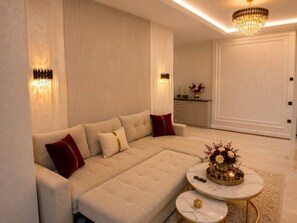 A modern living room with a large sofa, two side tables, a chandelier, and a decorative vase. - Premium Apartment | 5 Min to Airport (Тоshkent)