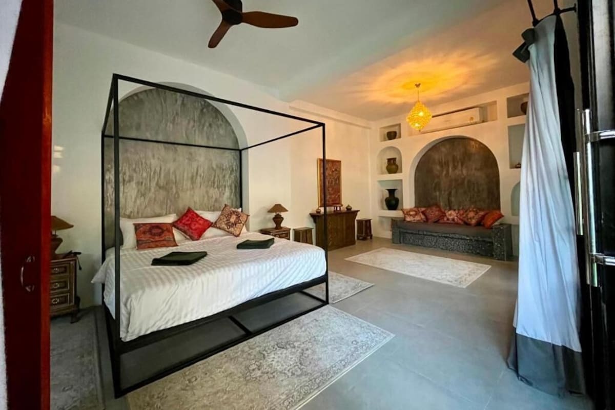 A bedroom with a four-poster bed, a ceiling fan, and a fireplace.