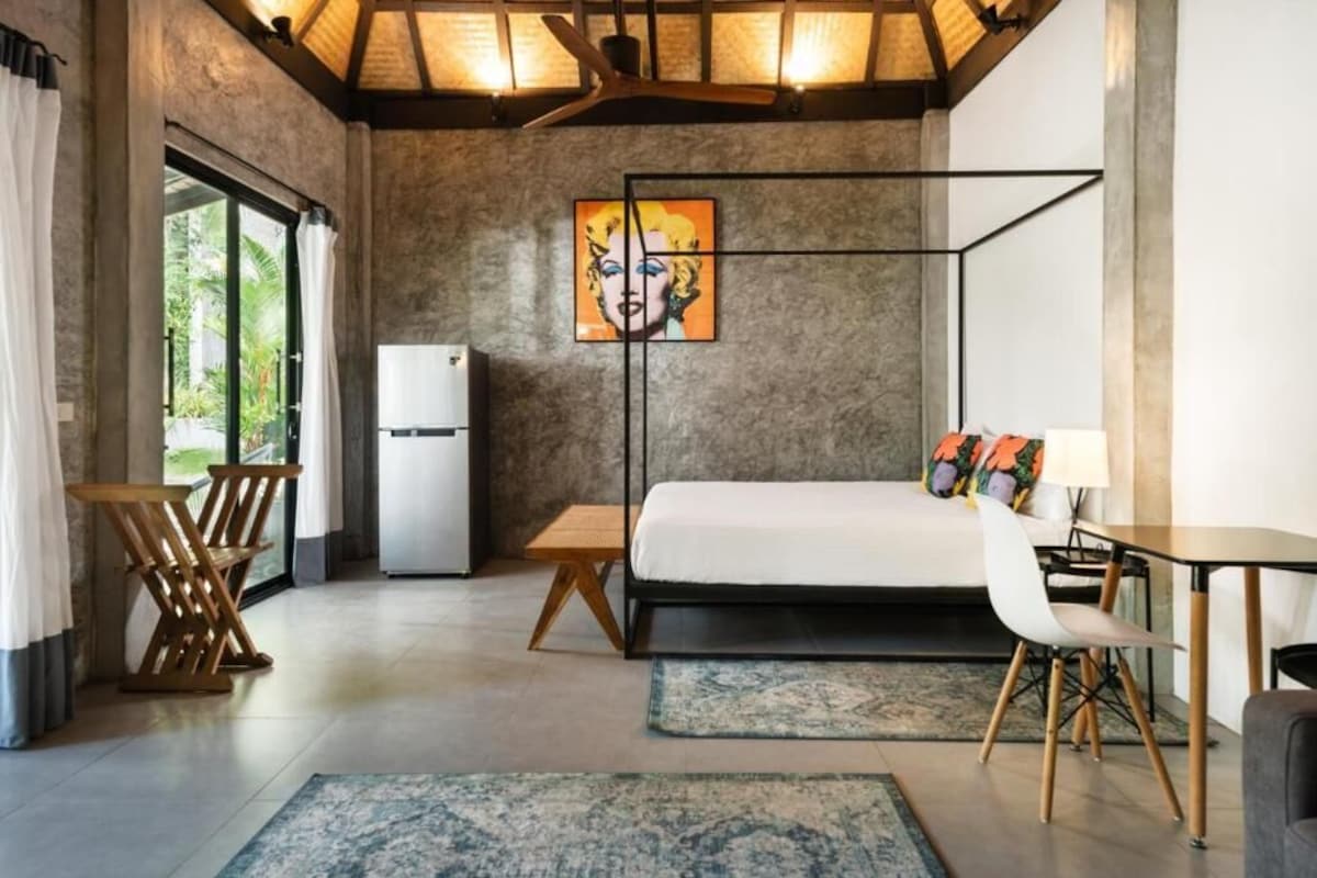 A modern bedroom with a bed, a desk, a chair, and a painting on the wall.