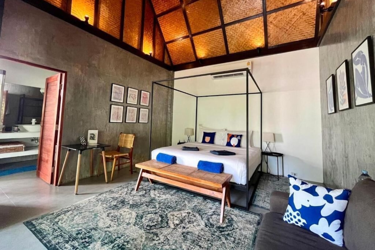 A modern bedroom with a four-poster bed, a bench, a sofa, and a dining area with chairs.