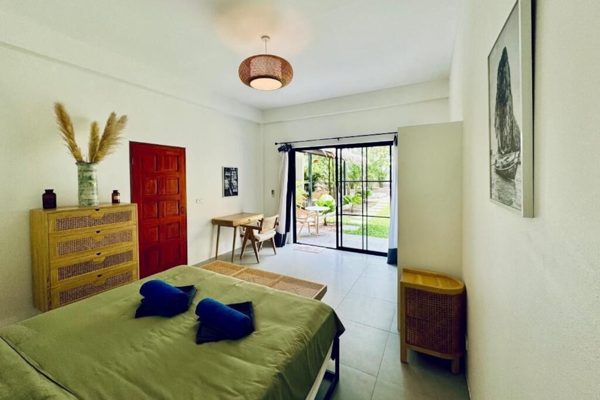 A bedroom with a bed, a dresser, a door, a window, and a view of the outdoors.