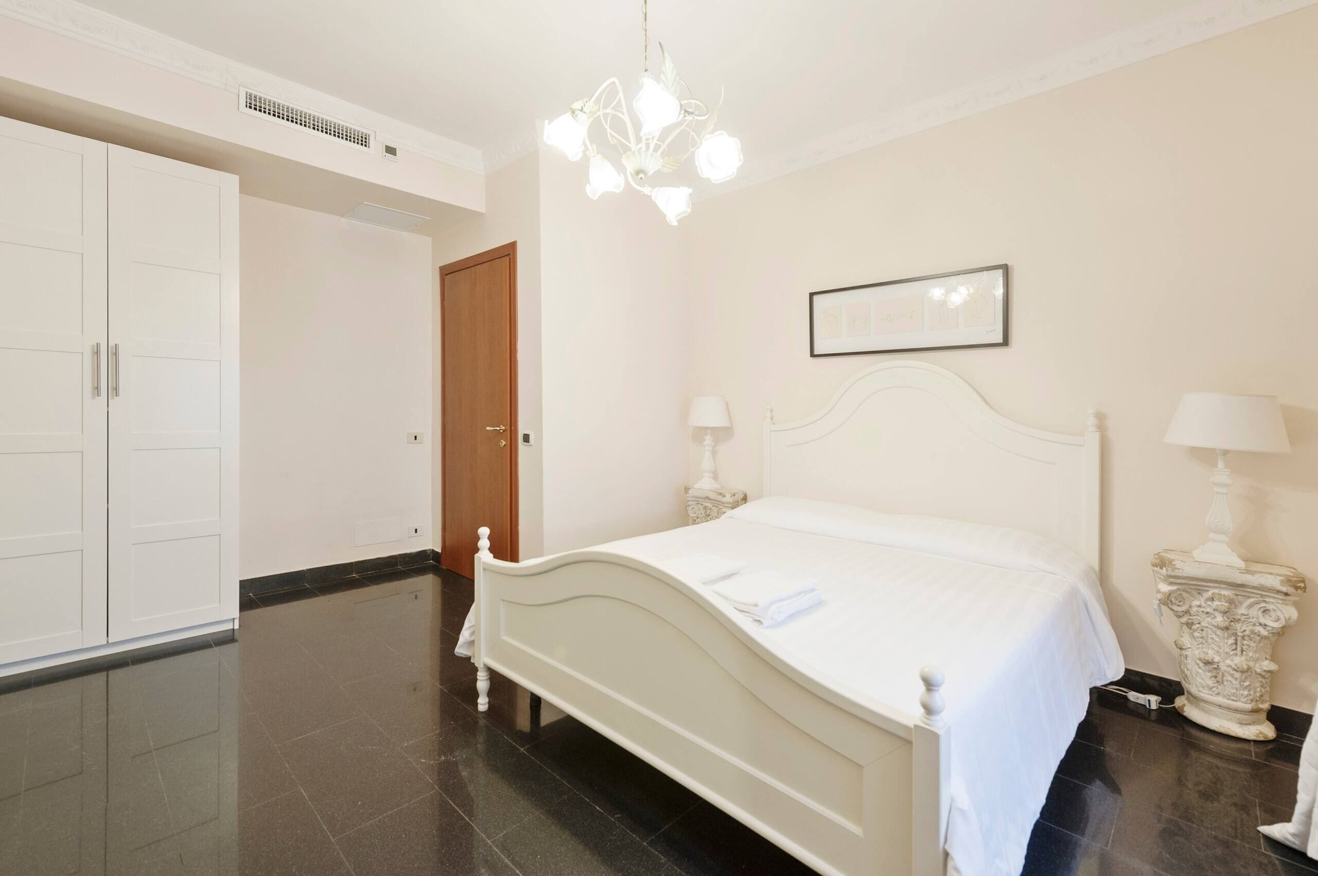 Un dormitorio con cama, lámparas de noche, armario y puerta.