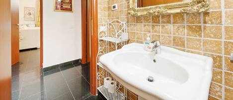 A bathroom with a white sink, a gold-framed mirror, and a tiled wall.