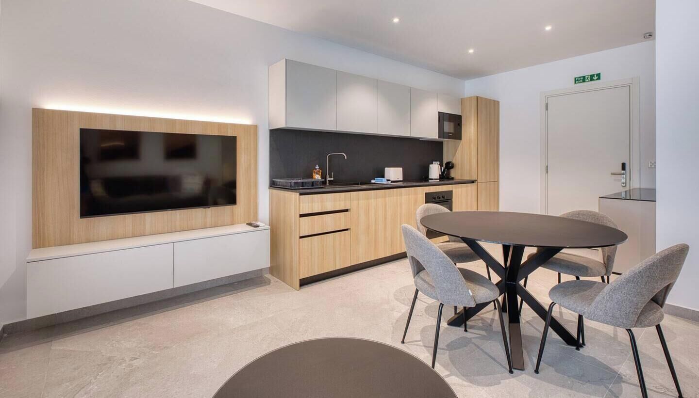Una cucina moderna con TV a schermo piatto, mobili in legno, un tavolo da pranzo rotondo con quattro sedie e una piccola isola con lavello.