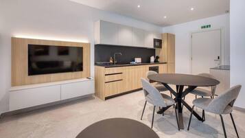 Una cucina moderna con TV a schermo piatto, mobili in legno, un tavolo da pranzo rotondo con quattro sedie e una piccola isola con lavello.