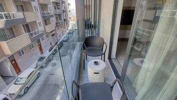 A balcony with two chairs and a small round table, overlooking a street with parked cars and buildings.