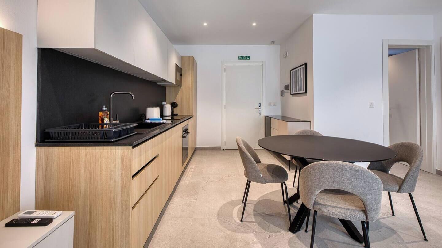 A modern kitchen with a black countertop, wooden cabinets, and a round table with four chairs.