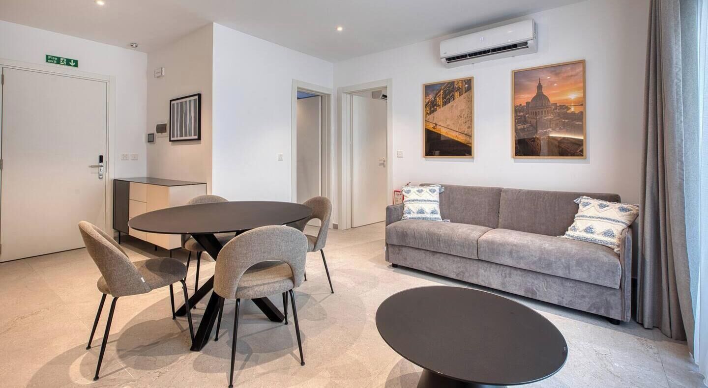 A modern hotel room with a dining area, a sofa, and two wall-mounted artworks.