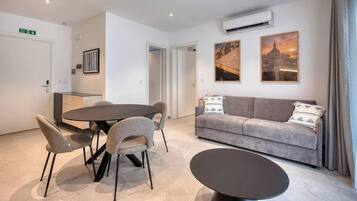 A modern hotel room with a dining area, a sofa, and two wall-mounted artworks.