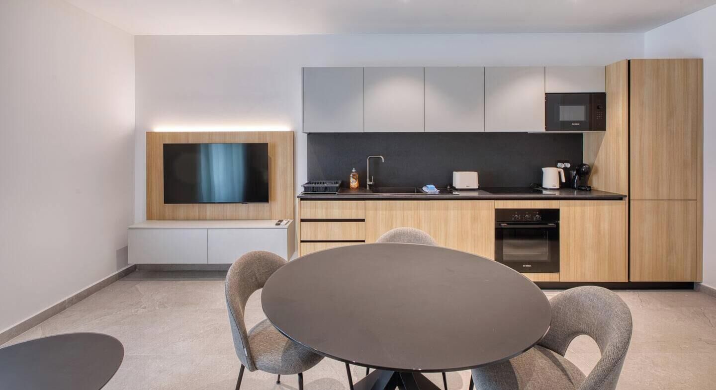 A modern kitchen with a flat-screen TV, a dining table with chairs, and built-in appliances.