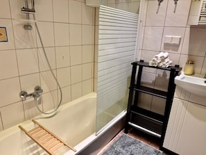 A bathroom with a glass-enclosed shower, a wooden shelf with towels, and a toilet. - Pilies23 Old Town Luxury Apartment (Vilnius)