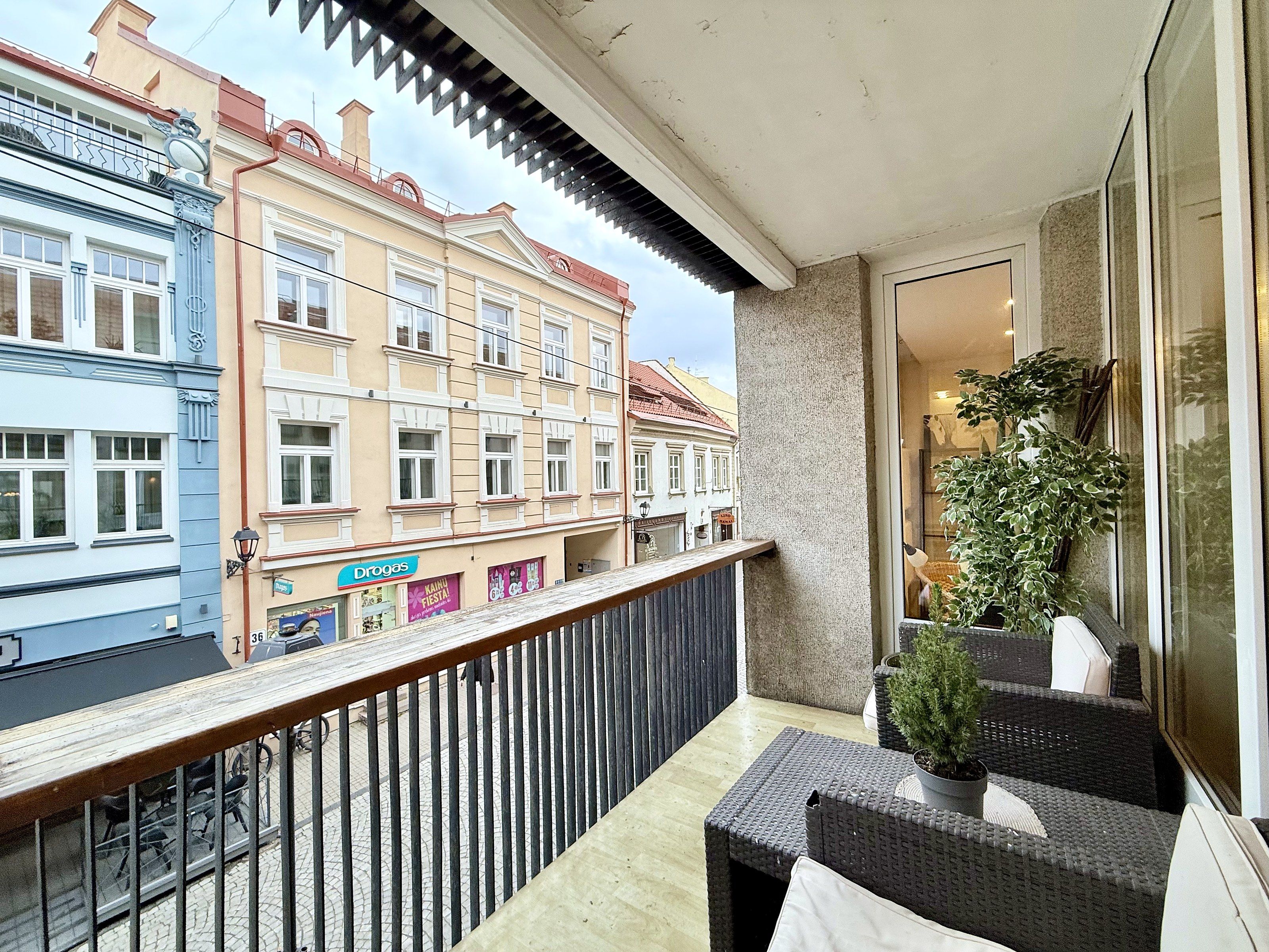 A balcony with wicker furniture, a potted plant, and a view of adjacent buildings.