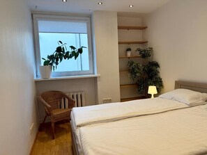 Un dormitorio con una cama, una silla, un ventanal con plantas y estanterías empotradas.
